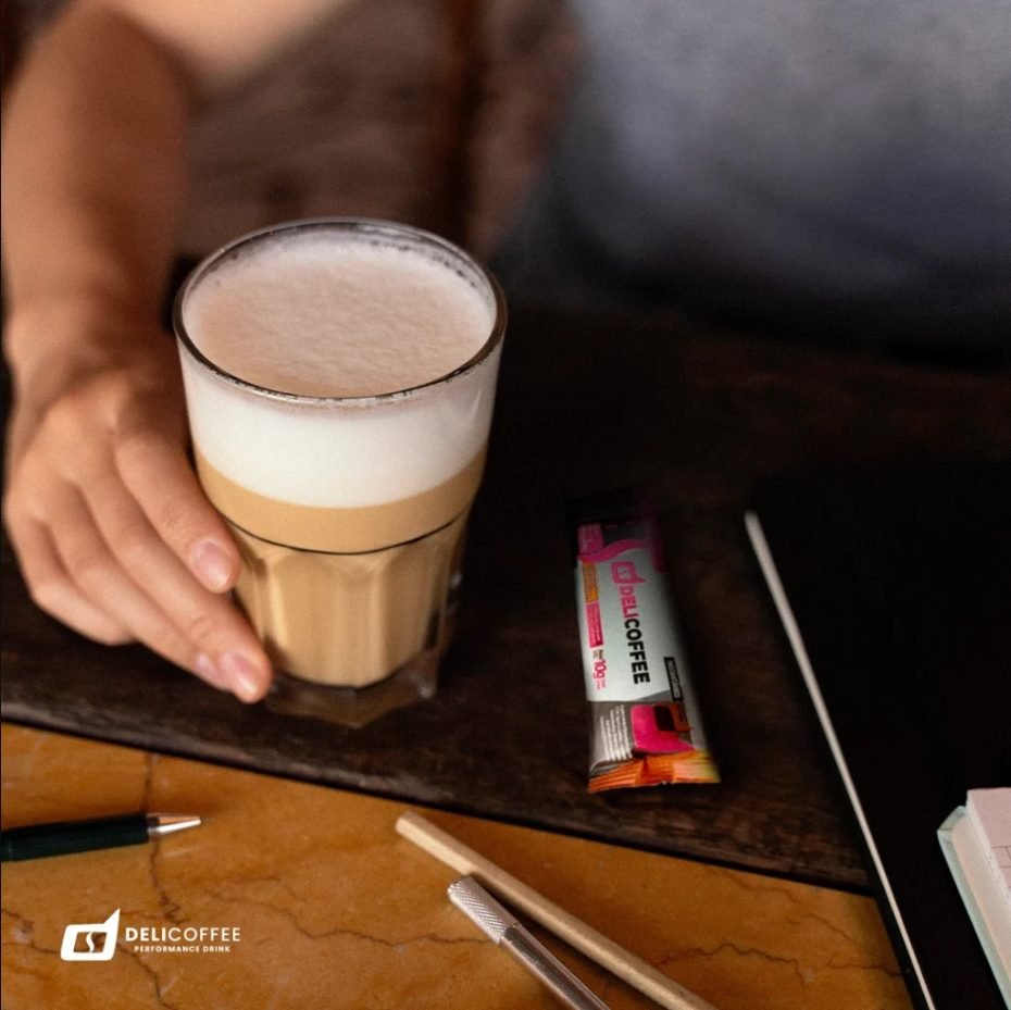 Copo de café com leite ao lado de um sachê DeliCoffee